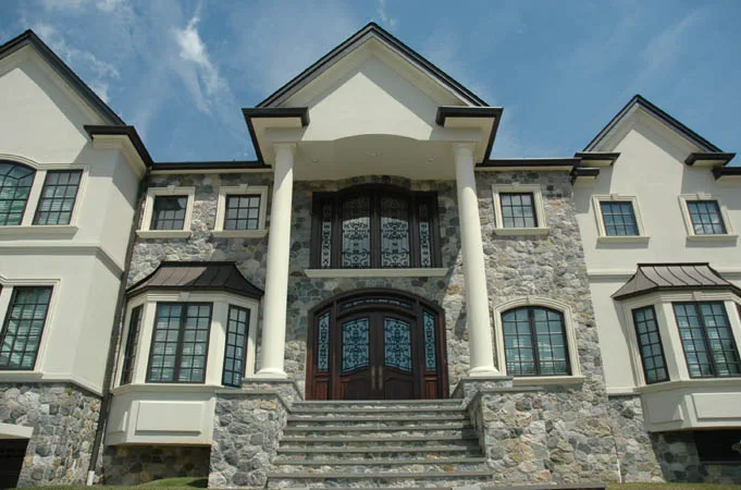 Stone and stucco house with arched wood entry doors at the top of wide stone steps