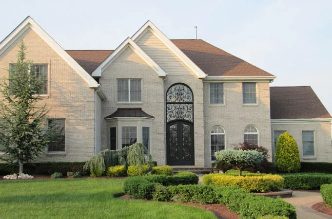 Light brick house with a tall arched iron-grille entry and transom behind a landscaped lawn
