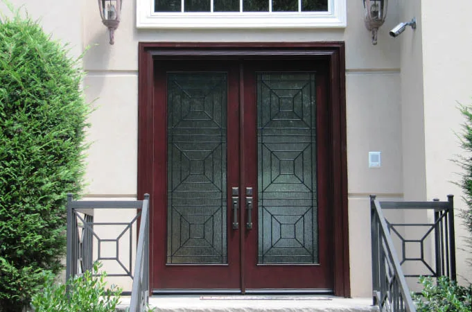 Dark red wood double doors with geometric leaded glass between modern metal railings