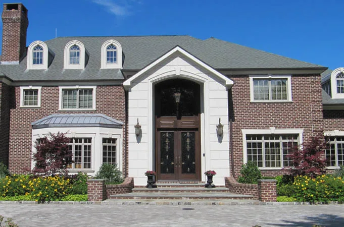 Brick house with wood double doors under a white arched entry surround