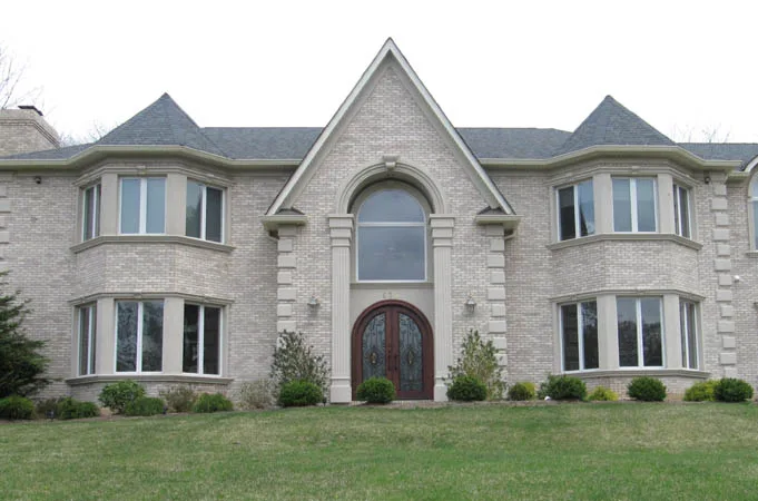 Light brick house with arched wood double doors under a tall arched window