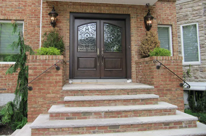 Wood double doors with iron-grille glass at the top of brick and stone steps