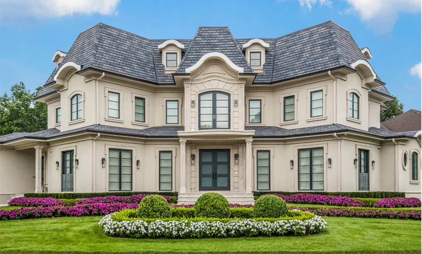 Stucco house with dark glass double doors behind round flower beds