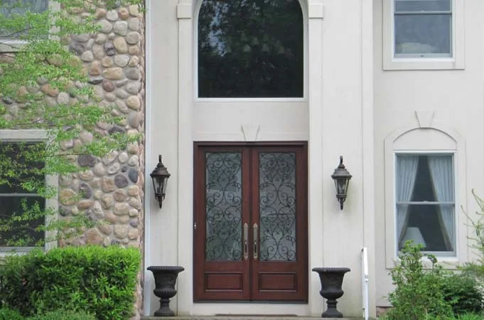 Wood double doors with iron-grille glass between two wall lights and urns