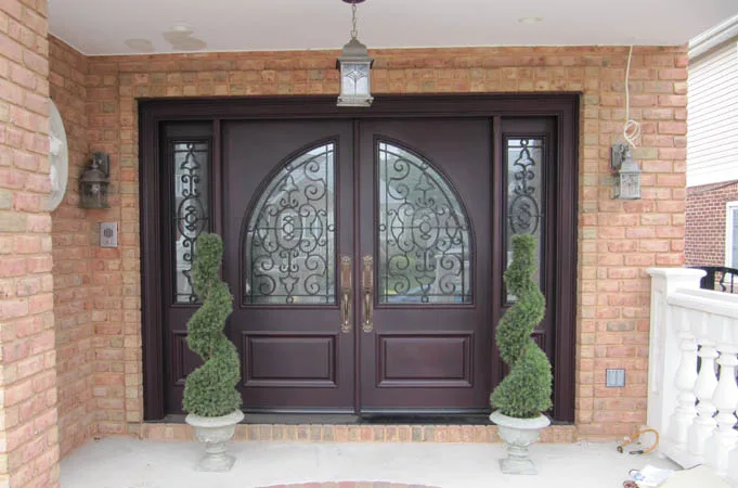 Wood double doors with arched iron-grille glass and sidelights, flanked by spiral topiaries