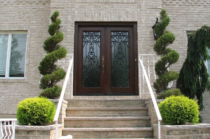 Wood double doors with iron-grille glass at the top of stone steps between spiral topiaries