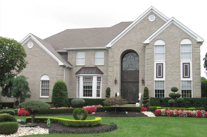 Brick house with a tall arched iron-grille entry behind a landscaped front garden