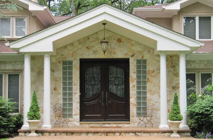 Wood double doors with iron-grille glass under a columned stone porch