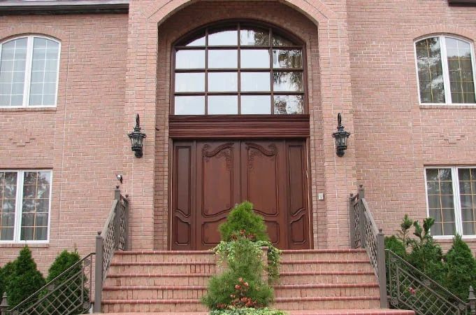 Carved wood double doors under a large arched window at the top of brick steps