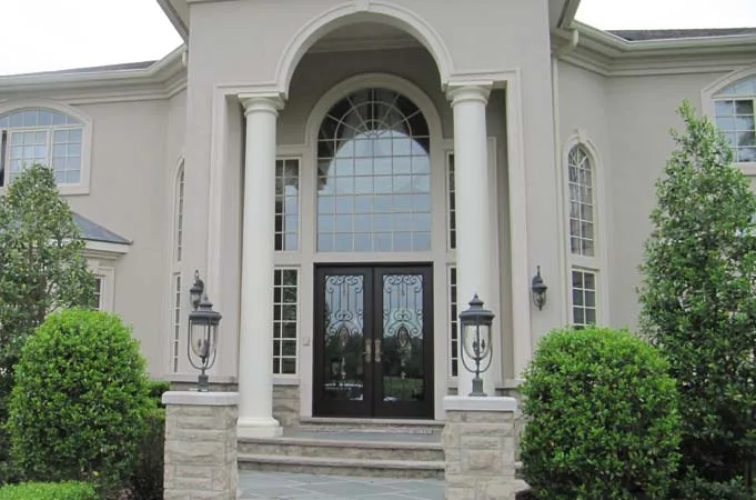 Black double doors with iron-grille glass under a tall arched window between columns
