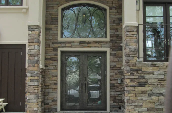 Iron double doors with scroll grilles under an arched transom in a stacked-stone wall
