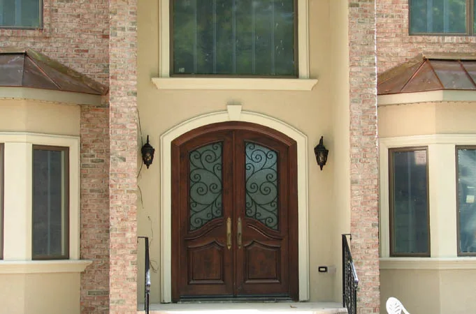 Arched wood double doors with iron-grille glass in a cream stucco entry