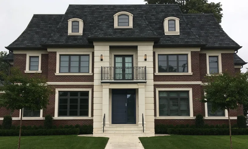 Brick and limestone house with a dark single entry door under a balcony