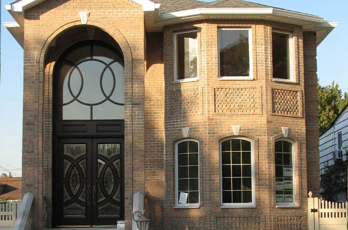 Brick house with dark double doors under a tall arched glass transom with a circle pattern