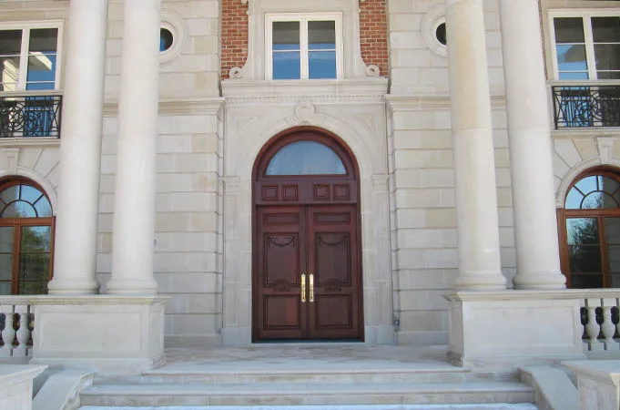 Arched wood double doors with transom in a limestone facade between tall columns
