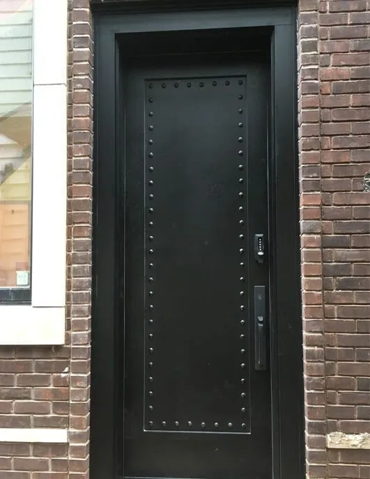Tall black door with rows of studs and a keypad, set in a brick wall