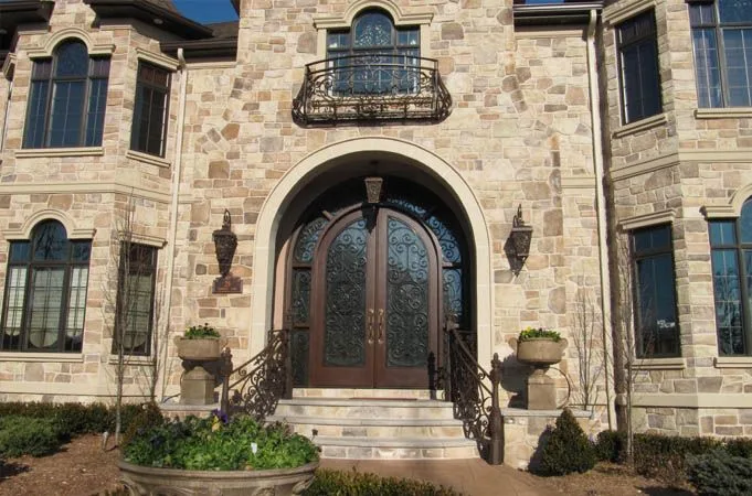 Arched wood double doors with iron grilles in a stone entry with curved railings