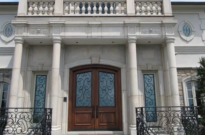 Arched wood double doors with iron-grille glass and matching sidelights between stone columns