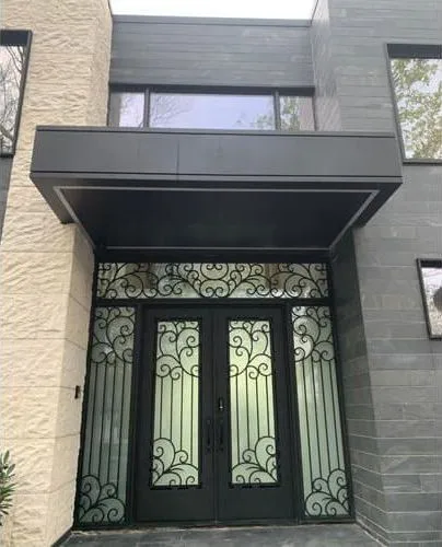 Black iron double doors with scroll grilles, sidelights and transom under a flat canopy