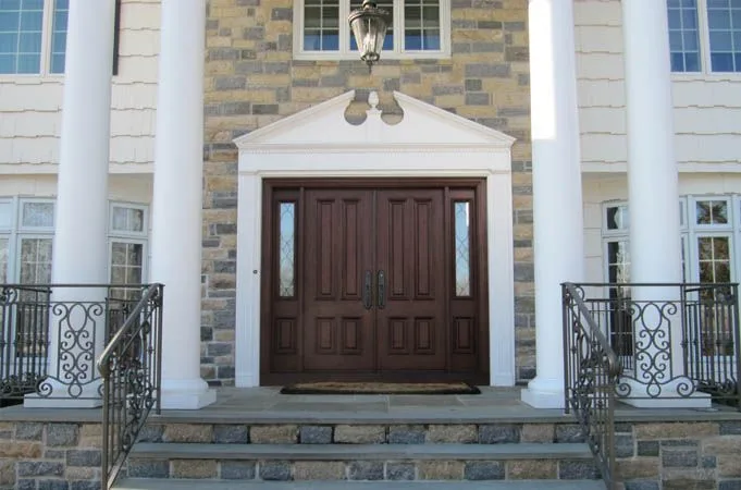 Raised-panel wood double doors with narrow sidelights under a white pediment