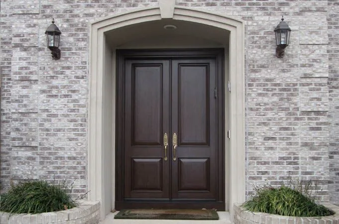 Dark raised-panel wood double doors in an arched stone surround, with wall lights