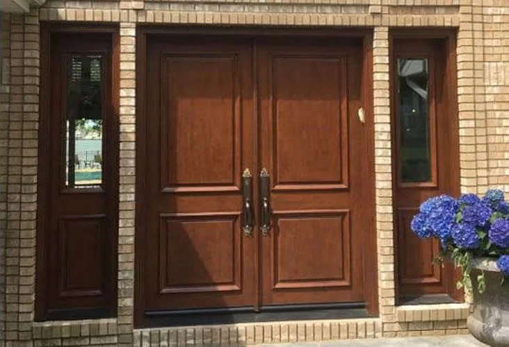 Raised-panel wood double doors with glass sidelights in a brick entry
