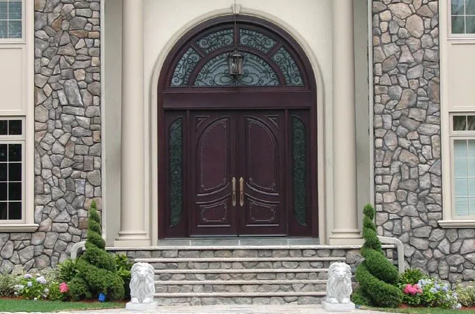 Carved wood double doors under an arched iron-grille transom, with lion statues on the steps