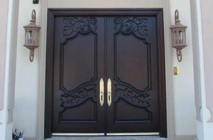 Dark carved wood double doors with scrollwork panels, flanked by wall lights