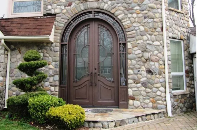 Arched dark wood double doors with glass inserts in a round fieldstone wall