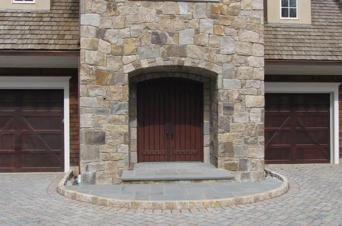 Plank-style wood double doors in an arched stone entry between two garage doors