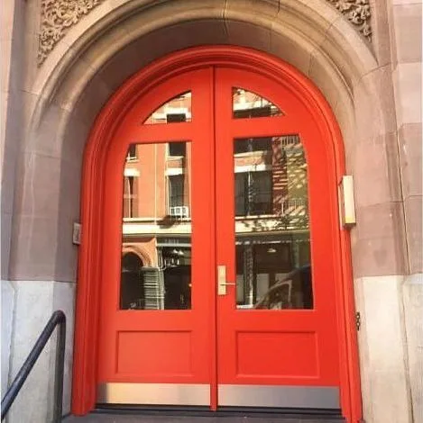 Arched red double doors with glass panes in a carved stone archway